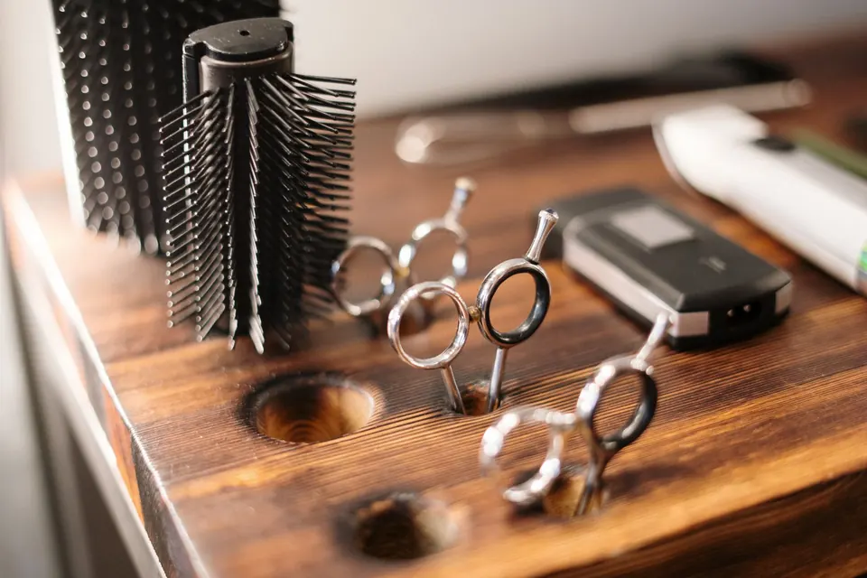 Barber scissors, a round brush and clippers laid out on a wooden station