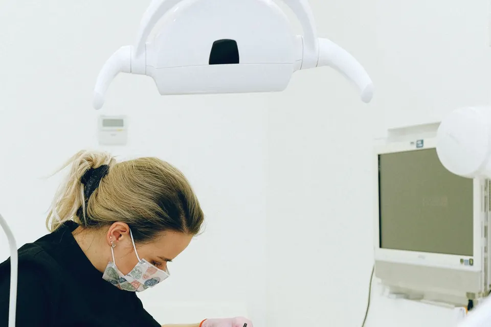 Dental professional in a mask working under a dental light in a bright treatment room