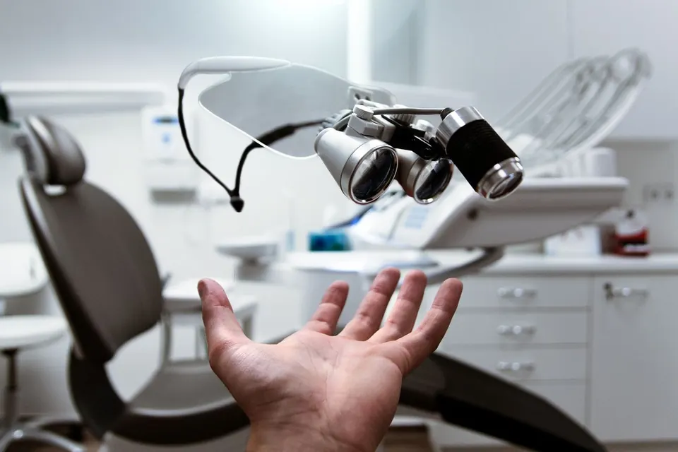 Dental loupes held above an open hand in an empty dental treatment room