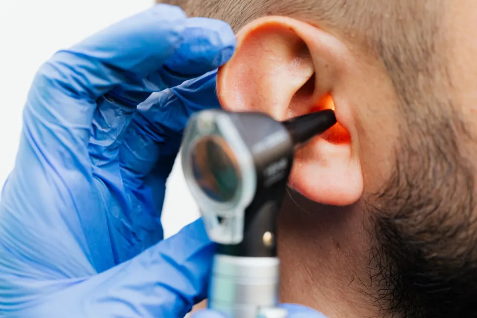 Gloved clinician examining a patient's ear with an otoscope