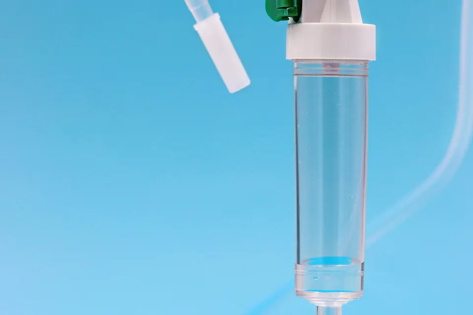 Close-up of an IV drip chamber and tubing against a plain blue background