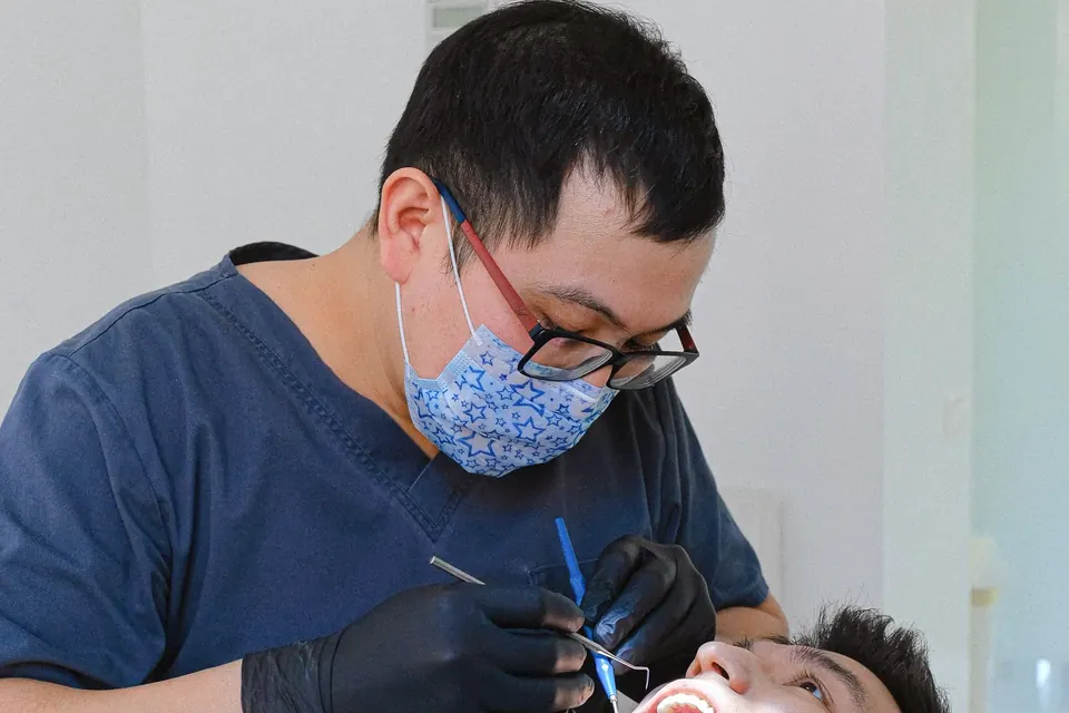 Dentist in glasses and a mask examining a patient's teeth with dental instruments