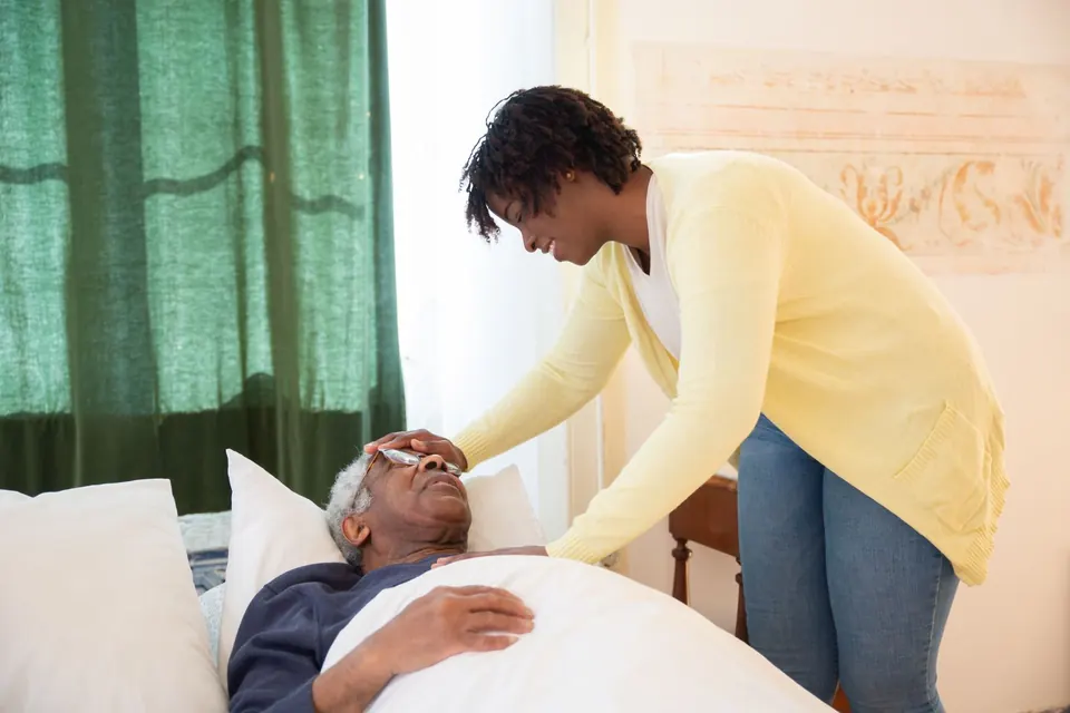 Carer checking on an older man resting in bed at home