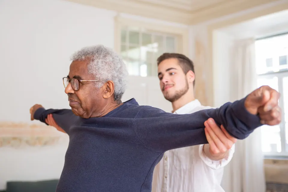 Physiotherapist guiding an older man through an arm exercise at home