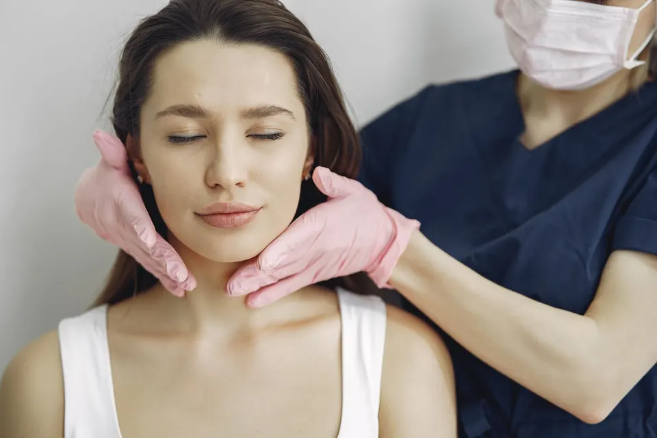 Clinician in a mask and gloves assessing a patient's jaw area before any treatment
