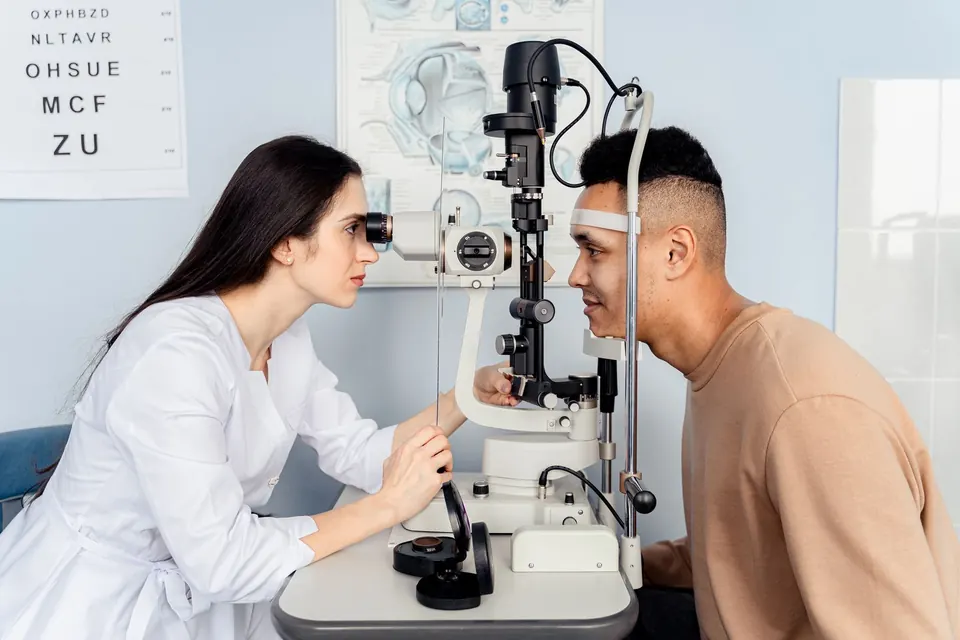Eye doctor examining a patient at a slit lamp in front of an eye chart
