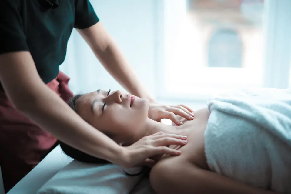 Massage therapist working on a customer's neck and shoulders, customer covered by a towel on a treatment bed