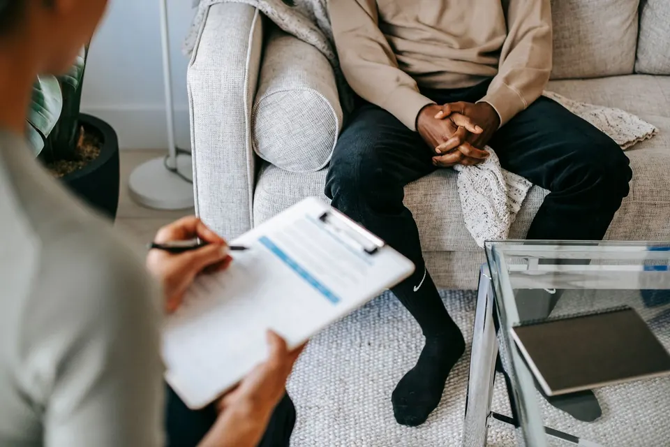 Therapist taking notes on a clipboard while a client sits on a sofa, faces not shown