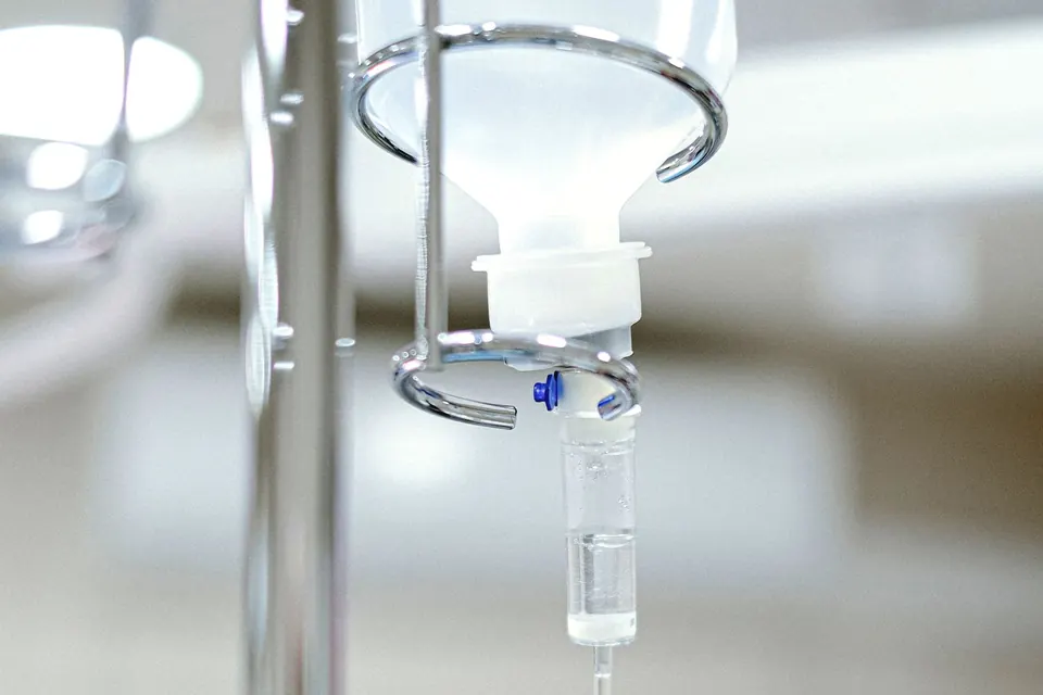 IV infusion bottle and drip chamber hanging on a stand in a bright clinic room