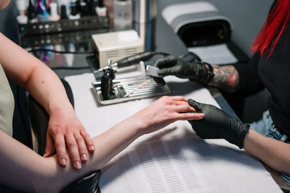 Nail technician in black gloves filing a customer's nails at a clean station with a sterilised tool tray