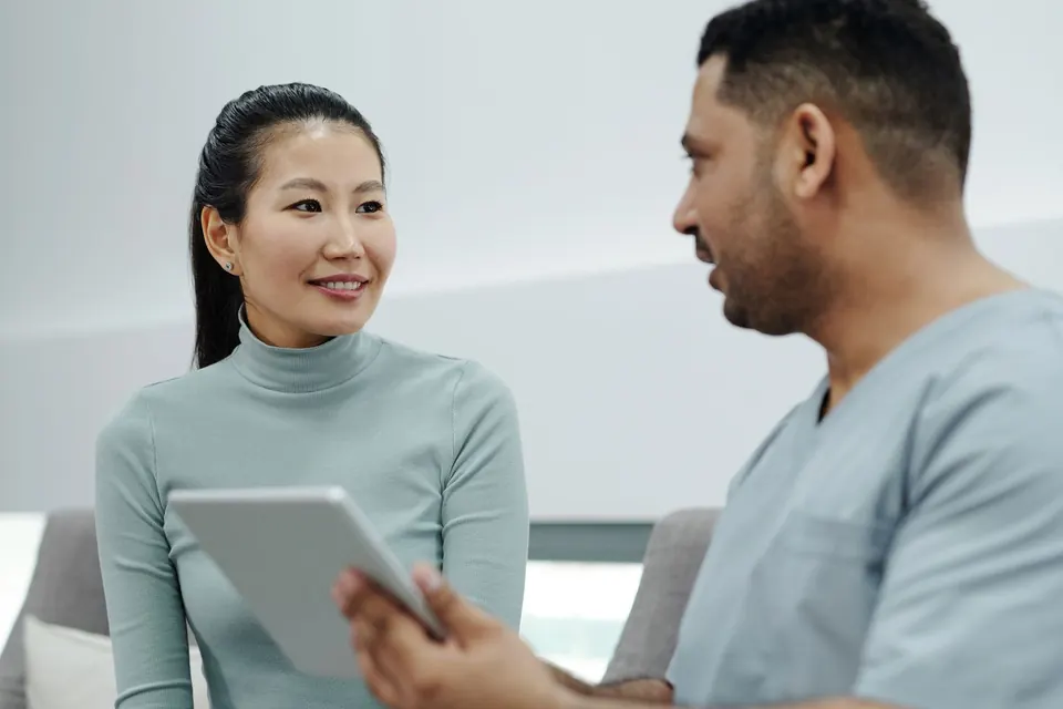 Surgeon in scrubs discussing a plan on a tablet with a patient in a clinic lounge