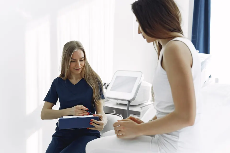 Clinician with a folder talking with a patient next to an aesthetic device in a bright treatment room
