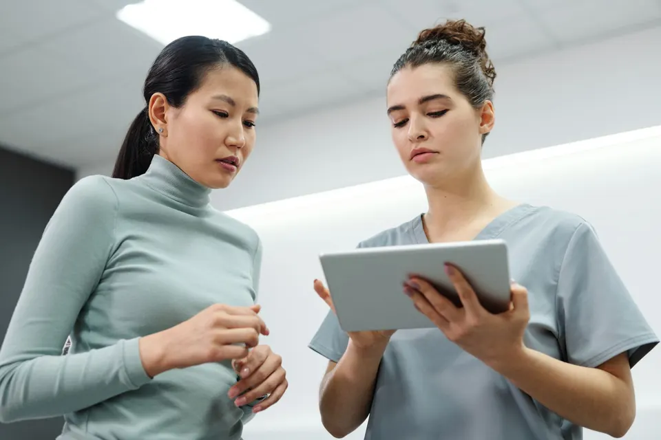 Clinician in scrubs explaining a plan on a tablet to a patient