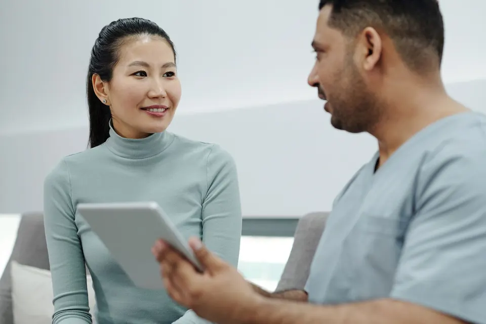 Doctor in scrubs talking a patient through information on a tablet in a consultation room